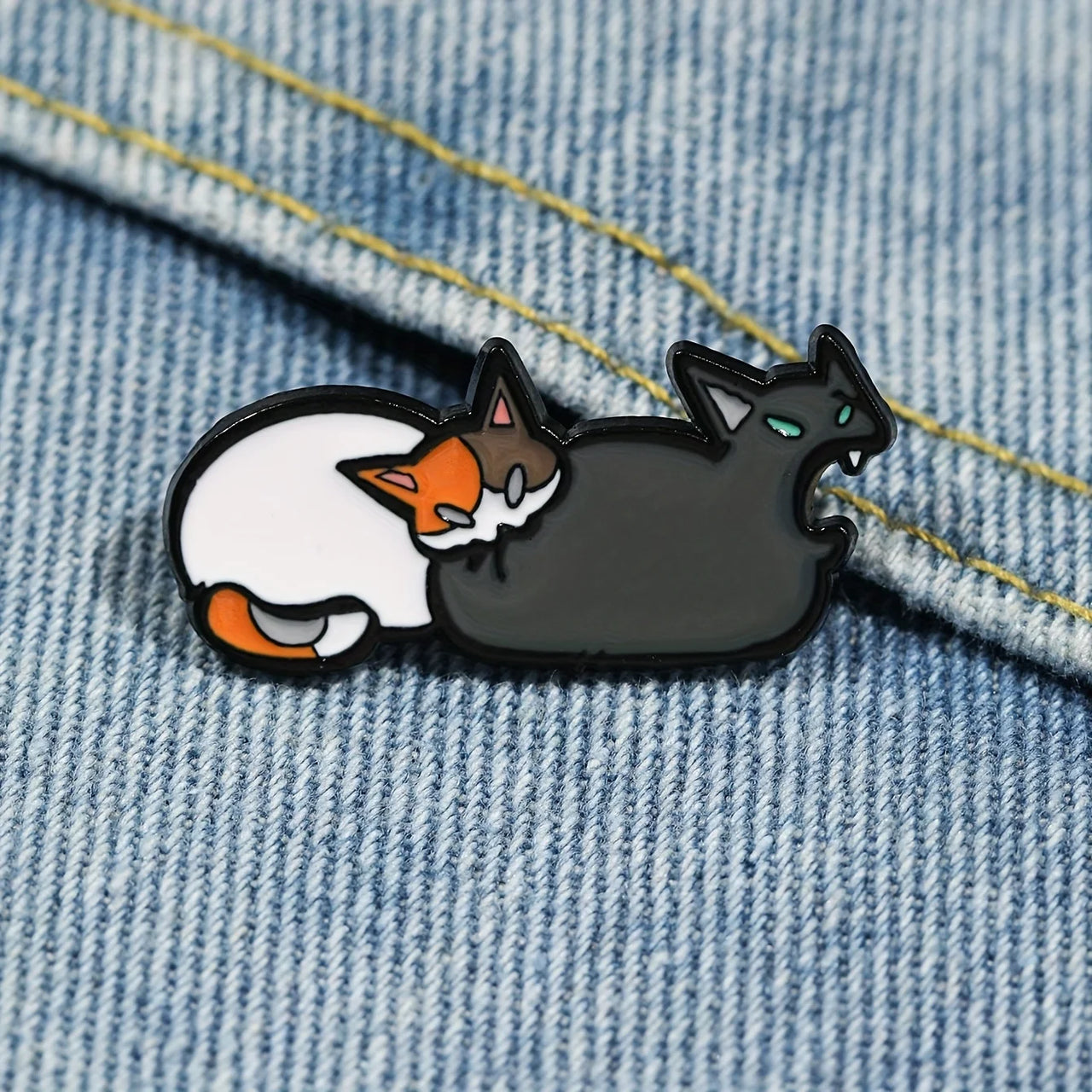 The Cute Feline Enamel Brooch by KittyNook Cat Co. features two cartoon cats cuddling on soft denim fabric.
