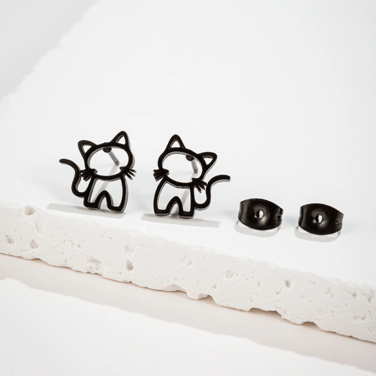 KittyNook Cat Co. KittyShine stainless steel black cat ear studs with backs, displayed on a white textured surface.