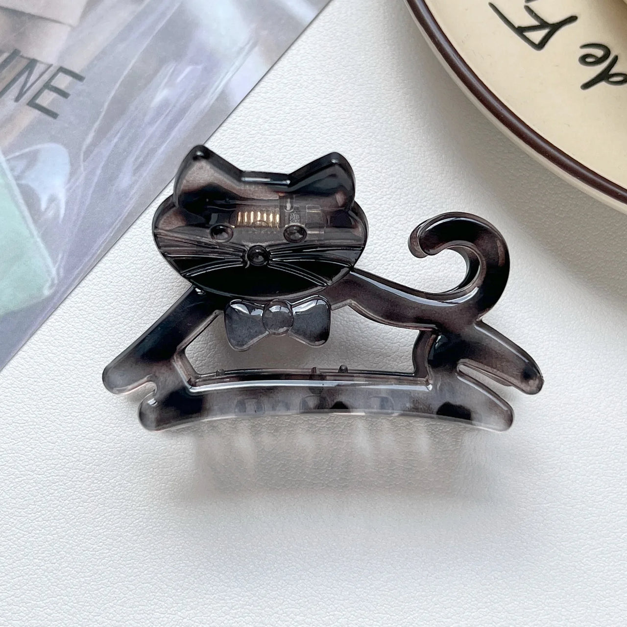 The Cute Cat Hair Claw by KittyNook Cat Co. with a bow tie, shown on a white surface beside a plate and magazine.
