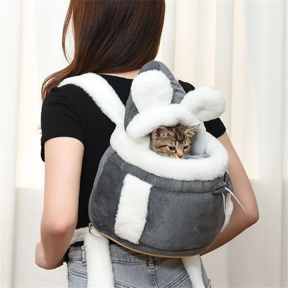 A woman carries The Stylish Pet Travel Bag by KittyNook Cat Co., a gray and white bunny-shaped pet carrier with a kitten inside.