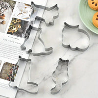 Thumbnail for Five KittyNook Cat Co. Cat Shape Cookie Cutter Set pieces sit on a counter beside a magazine, plate, and cookies.