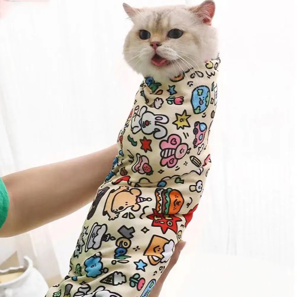 A cat peeks from the KittyNook Cat Co. Burrito Grooming Wrap, cozy in its cute, anti-bite cartoon-patterned swaddle.