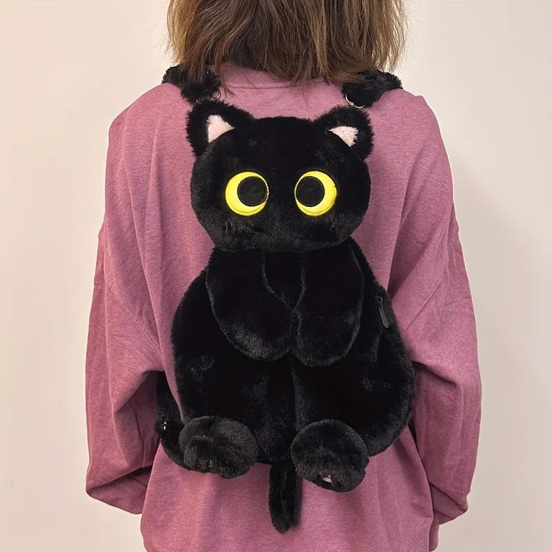 A person wears KittyNook Cat Co.'s Cute Big Eyes Plush Backpack—a black cat design—over a mauve sweater.