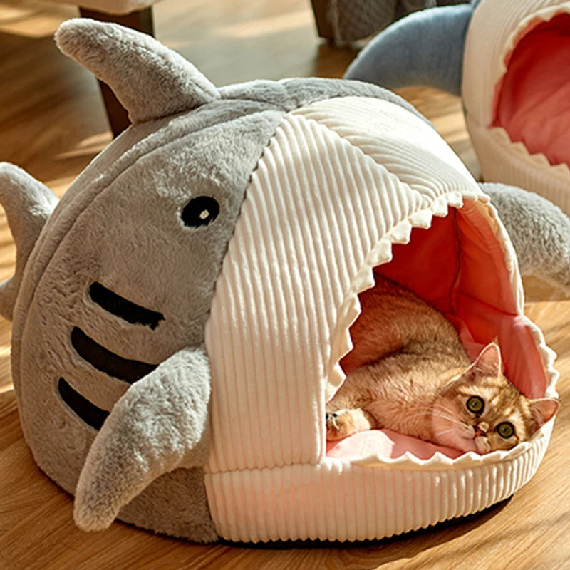 A cat peeks out of the KittyNook Cat Co. Shark-Shaped Cat Cave Bed’s open mouth.