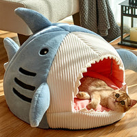 Thumbnail for A cat relaxes in the KittyNook Cat Co. Shark-Shaped Cat Cave Bed with an open-mouth design on a wooden floor.