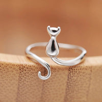 Thumbnail for The Cute Adjustable Silver Cat Ring by KittyNook Cat Co. features a curled tail and is shown on a wooden surface.