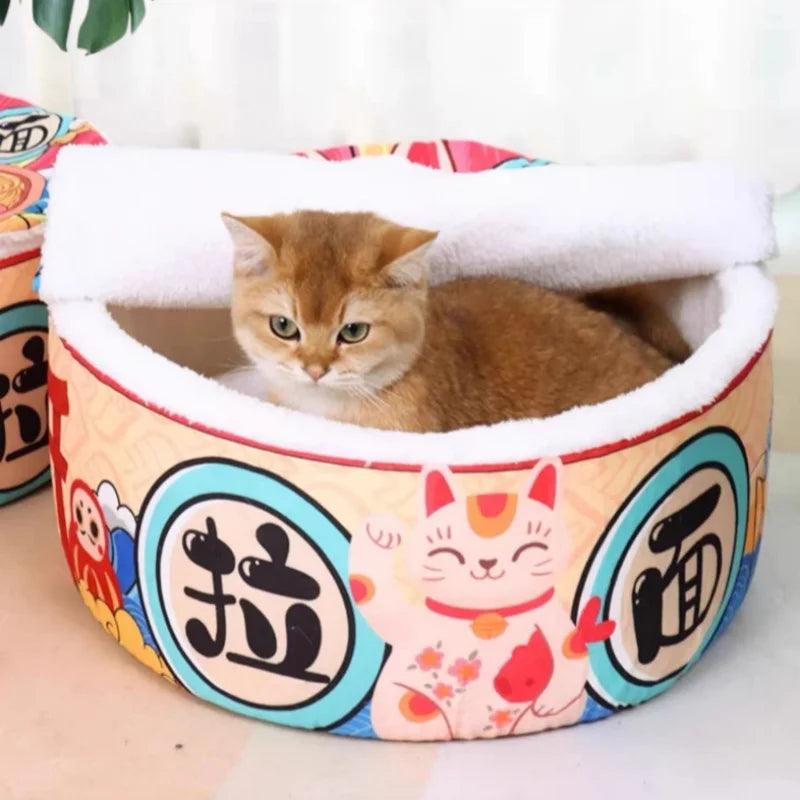 A brown cat sits inside the Giant Ramen Bowl Cat Bed by KittyNook Cat Co., shaped like a round ramen bowl.