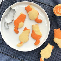 Thumbnail for Cat-shaped orange and white cookies made with KittyNook Cat Co.'s Cat Shape Cookie Cutter Set on a cooling rack.