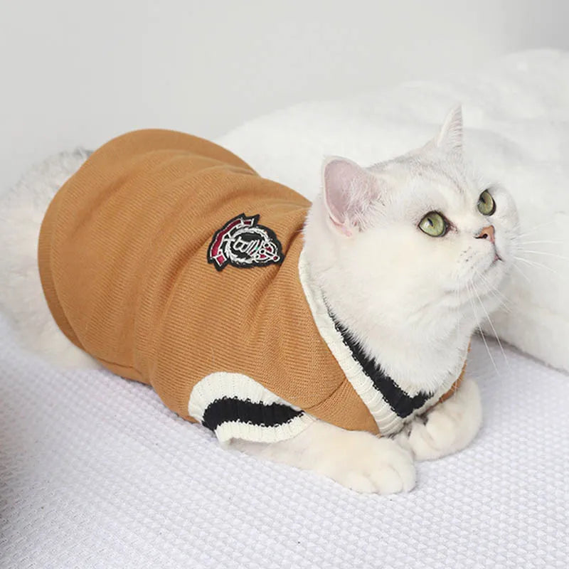 A white cat in a Cozy Fluff Cat Sweater by KittyNook Cat Co. lounges on a white textured surface, looking up.
