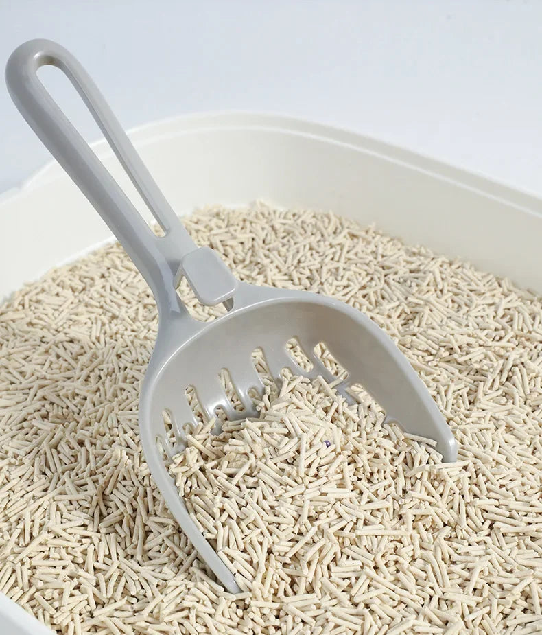 A KittyNook Cat Co. Curved Cat Litter Shovel sits in a box of odor-free, pellet cat litter.