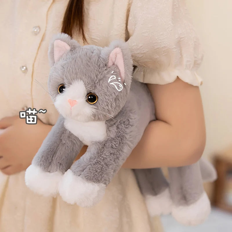 A person in a cream dress holds the Snuggle Soft Cat Plush Doll by KittyNook Cat Co., with large eyes and pink ears.