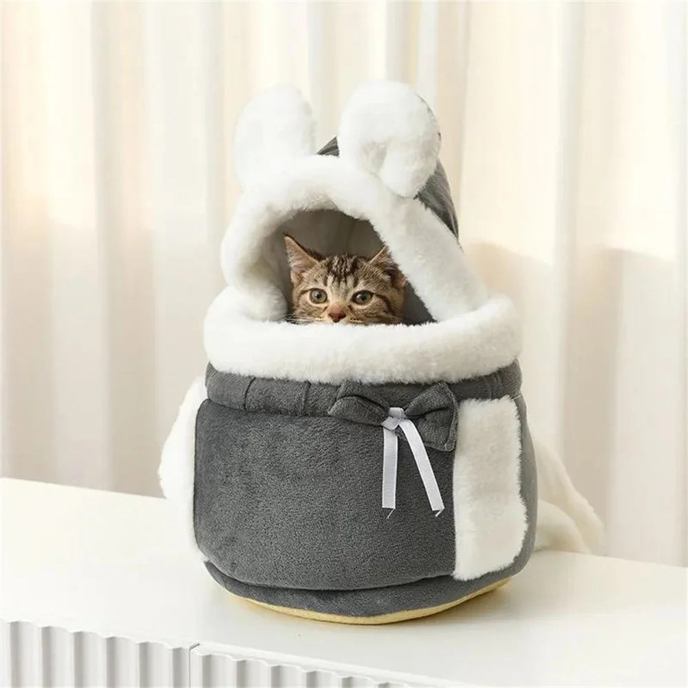 A tabby cat sits in The Stylish Pet Travel Bag by KittyNook Cat Co., a gray bunny-shaped plush pet carrier.