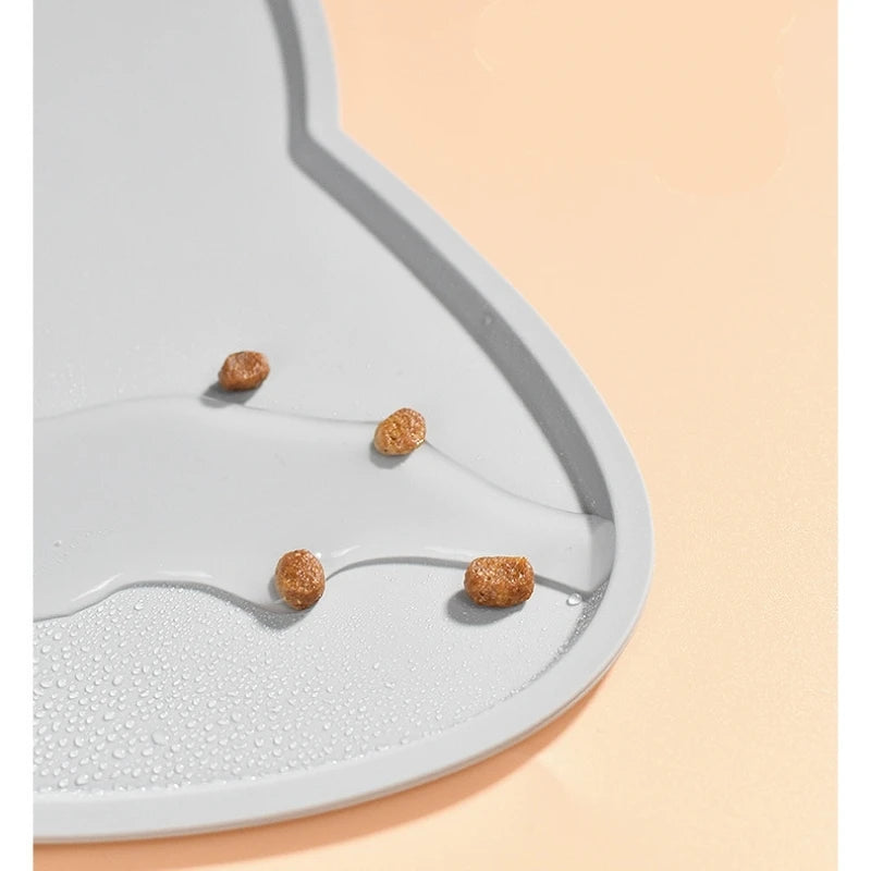 Four pieces of dry pet food on a KittyNook Cat Co. Silicone Pet Feeding Bowl with water droplets, peach background.