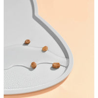 Thumbnail for Four pieces of dry pet food on a KittyNook Cat Co. Silicone Pet Feeding Bowl with water droplets, peach background.