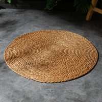 Thumbnail for KittyNook Cat Co. Natural Rattan Cat Scratcher on gray stone floor, an eco-friendly option with green leaves nearby.
