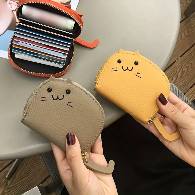 Two hands hold KittyNook Cat Co. Cute Multi-Card Cat Purses—one gray, one yellow—near an open wallet on a table.