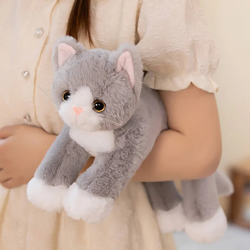 Person in a cream dress holds a KittyNook Cat Co. Snuggle Soft Cat Plush Doll with big eyes and pink ears.