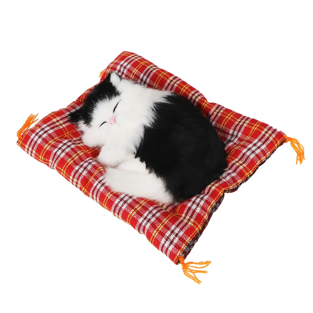 KittyNook Cat Co.’s Sleepy Kitten Plush Decoration is a cute home accessory, curled up on a red plaid cushion.