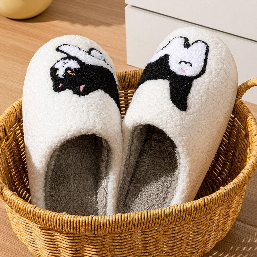 CozyPaws Cute Cat House Slippers by KittyNook Cat Co., with black and white designs, in a basket on a wooden floor.